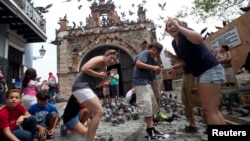 FILE - Tourists react to a flock of pigeons as they visit Parque de las Palomas in San Juan, Puerto Rico, July 18, 2015. 