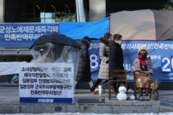 FILE - A protester sits next to a statue symbolizing a wartime sex slave to demand full compensation and an apology for wartime sex slaves near the Japanese Embassy in Seoul, South Korea, Jan. 8, 2021.