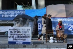 Seorang pengunjuk rasa duduk di sebelah patung yang melambangkan perbudakan seks di masa perang di dekat Kedutaan Besar Jepang di Seoul, Korea Selatan, Jumat, 8 Januari 2021 (Foto: AP)