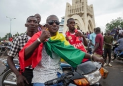 A man wears a national flag as he celebrates with others in the streets in the capital Bamako, Mali, Aug. 18, 2020.