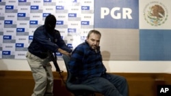 Jesus Reynaldo Zambada Garcia, known as Jesus "The King" Zambada, a leader in the Sinaloa drug cartel, is pushed in a chair by a masked police officer as Garcia is presented to the press in Mexico City, Wednesday, Oct. 22, 2008. (AP Photo/Alexandre Meneg