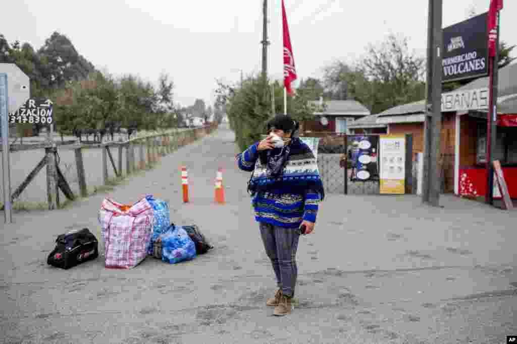 A woman holds a mask to her face as she stands with her belongings before evacuating the town of Ensenada, Chile after the Calbuco volcano erupted, April 23, 2015