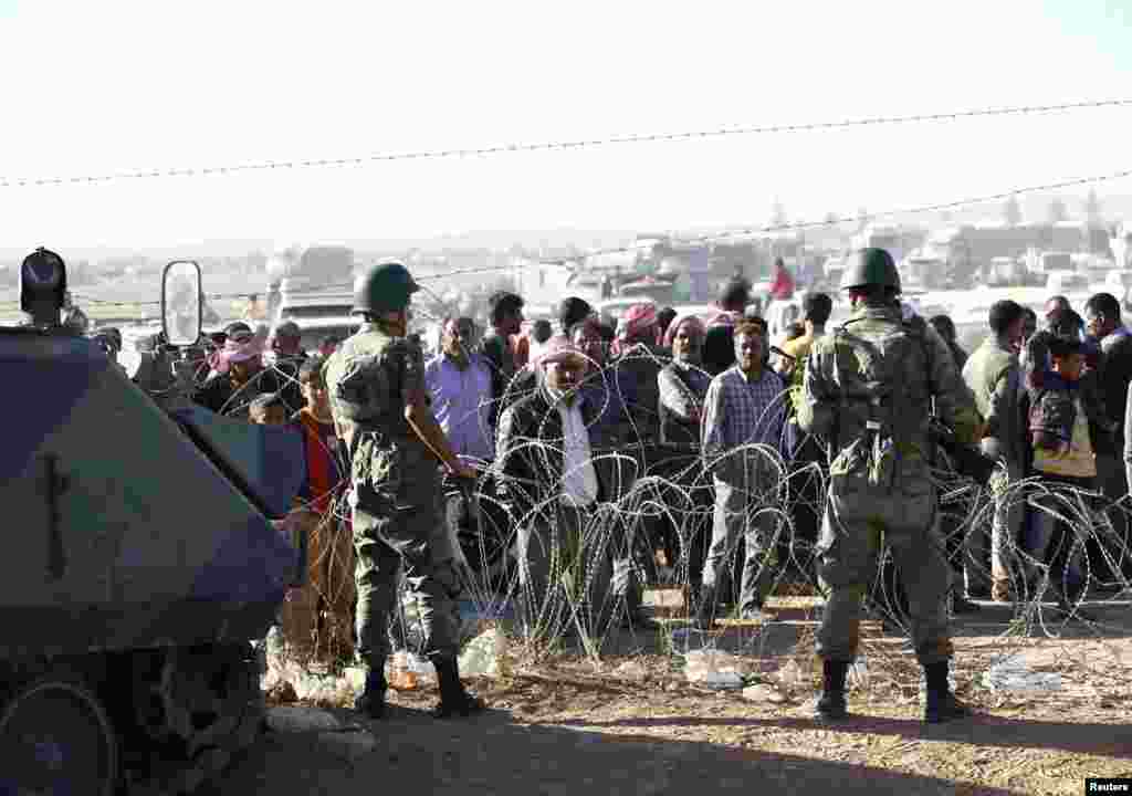 Syrian Kurds wait behind a border fence near the southeastern town of Suruc in Sanliurfa province, Sept. 22, 2014.