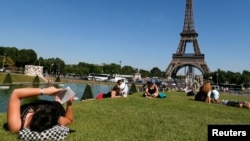 FILE - A woman reads a book as she rests in a public garden near the Eiffel Tower on a hot summer day in Paris, July 3, 2014. 