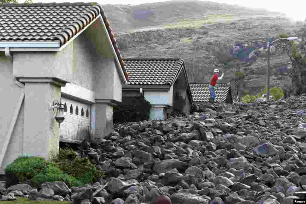 A worker stands on top of a pile of rock and mud after a mudslide overtook at least eight homes during heavy rains in Camarillo Springs, California. The large storm moved south overnight, requiring evacuation orders in areas prone to floods and mud flows.