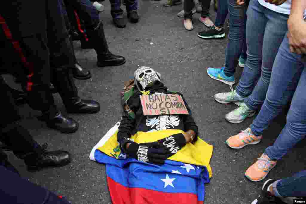 An opposition supporter wearing a costume and a placard that reads &quot;Bullets no, food yes&quot; lies on the floor in front of riot policemen during a rally against President Nicolas Maduro&#39;s government in Caracas, Venezuela.