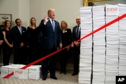 President Donald Trump speaks during an event on federal regulations at the White House, Dec. 14, 2017, in Washington. The large collection of paper at right was said to represent the size of the federal regulatory code, while the smaller stack at left was meant to represent the amount of federal regulation that existed in 1960.