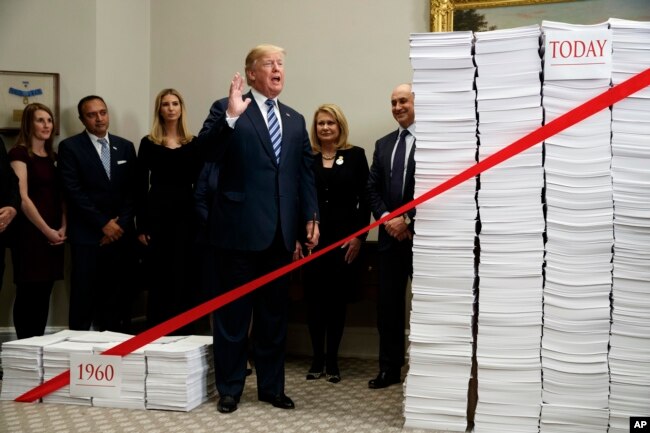 President Donald Trump speaks during an event on federal regulations at the White House, Dec. 14, 2017, in Washington. The large collection of paper at right was said to represent the size of the federal regulatory code, while the smaller stack at left was meant to represent the amount of federal regulation that existed in 1960.