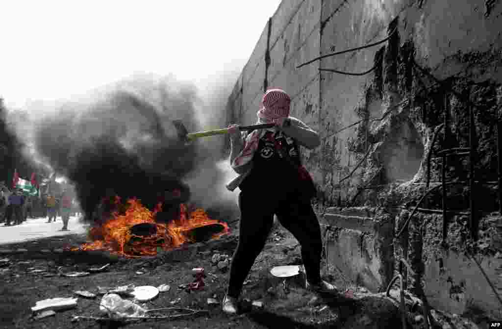 A female Palestinian demonstrater uses an axe to try and destroy a part of the Israeli controvertial separation wall separating the West Bank city of Abu Dis from east Jerusalem, during clashes with Israeli security forces.