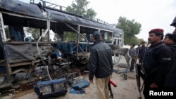 Security officials stand near a damaged police bus at the site of an explosion in Karachi, Feb. 13, 2014. 