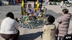 People gather around a makeshift memorial in front of portraits of late Israeli hostages Shiri, Ariel, and Kfir Bibas, as well as Oded Lifshitz at Hostages Square in Tel Aviv on Feb. 25, 2025, a day ahead of the Bibas family funeral.