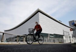 FILE - A man wearing a protective mask amid COVID-19 outbreak cycles past Ariake Arena in Tokyo, Japan, Apr. 8, 2021.