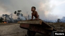 FILE - Jose, 2, plays while a fire burns a tract of Amazon jungle as it is cleared by loggers and farmers near Porto Velho, Brazil, Aug. 27, 2019. 