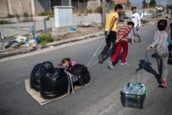 A child sits between plastic bags as migrants pull their belongings in Kara Tepe, near Mytilene, the capital of the northeastern island of Lesbos, Greece, Sept. 17, 2020.