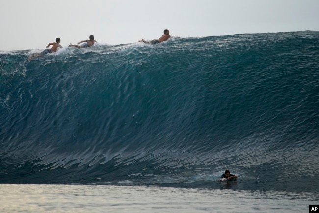 Surfers paddle over the top of a wave in Teahupo'o, Tahiti, French Polynesia, Sunday, Jan. 13, 2024. (AP Photo/Daniel Cole)