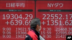 A man walks past an electronic stock board showing Japan's Nikkei 225 and New York Dow Jones index, at a securities firm in Tokyo, Japan, March 27, 2020.