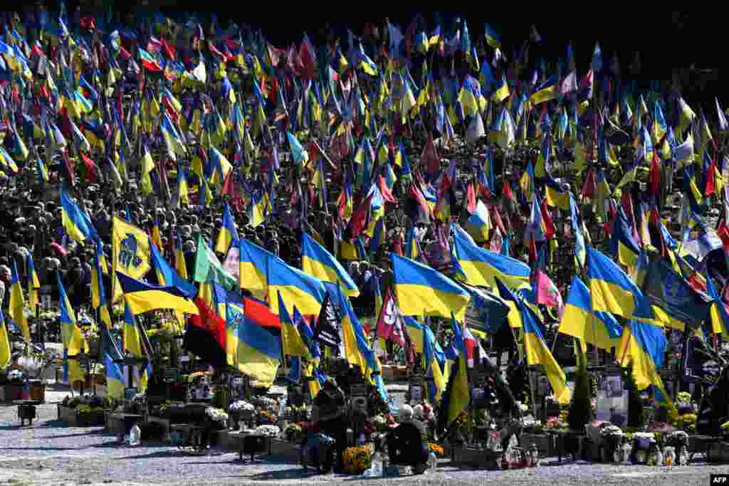 Warga setempat mengibarkan bendera selama upacara pemakaman prajurit Ukraina Volodymyr Pugolovko, Yuriy Shumalo dan Yuriy Cheliapin di Pemakaman Militer Lychakiv di Lviv, di tengah invasi Rusia di Ukraina. (AFP)&nbsp;