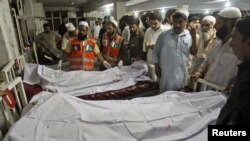 Polisi dan petugas rumah sakit berdiri dekat jenazah korban bom mobil di Peshawar, Pakistan. (Foto: Reuters)