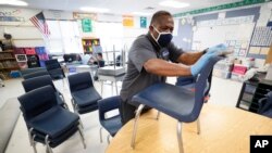 Des Moines Public Schools custodian Tracy Harris cleans chairs in a classroom at Brubaker Elementary School in Des Moines, Iowa, July 8, 2020.