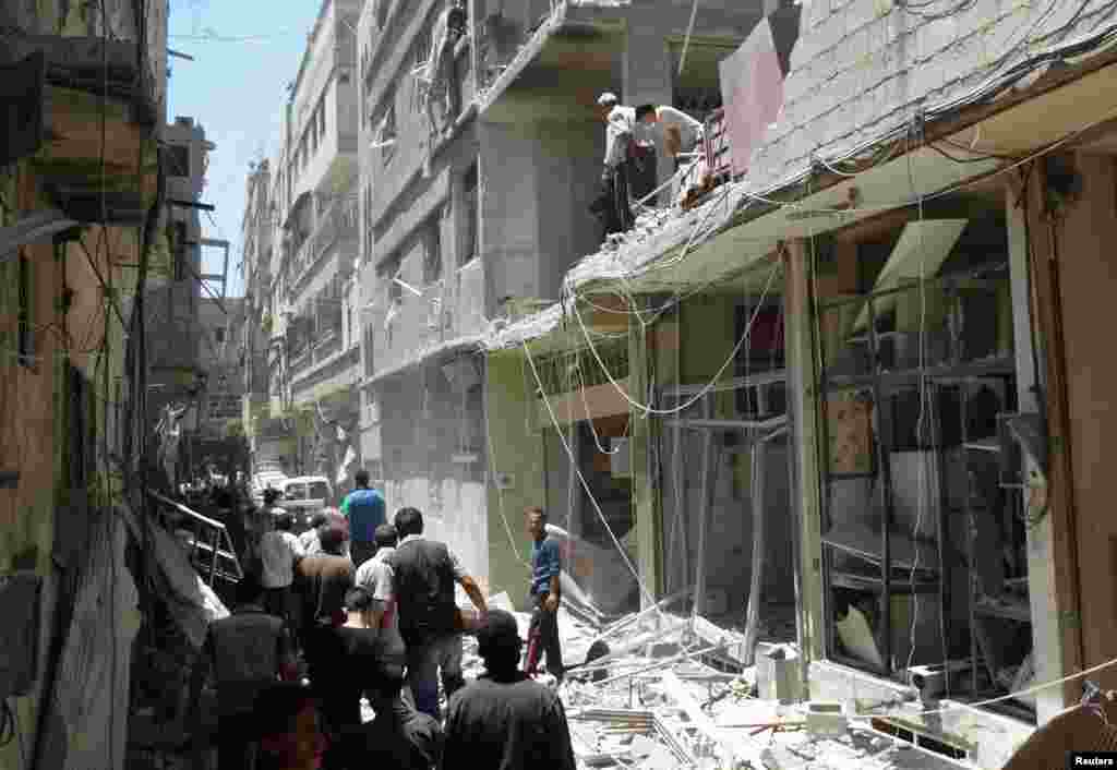 Men inspect the damage at a site hit by what activists said was an airstrike by forces loyal to Syria's President Bashar al-Assad at the Damascus suburb of Saqba, June 18, 2014. 