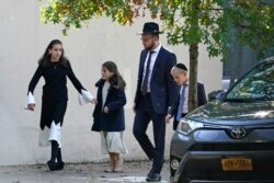 A man walks with his family, Sunday, Oct. 4, 2020, in the Borough Park neighborhood of New York. New York Gov. Andrew Cuomo says he’s ordering schools in certain New York City neighborhoods closed within a day to slow a flare-up of the coronavirus.