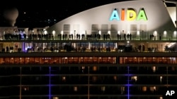 People stand on the deck of the German cruise ship AIDAnova, docked in Lisbon, shortly before midnight, Dec. 31, 2021.