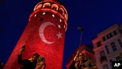 People take photos at the iconic Galata Tower, illuminated in Turkish flag colors, in Istanbul, July 30, 2016. Dozens of staff at Turkey's highest court have been suspended from their jobs as part of the crackdown in the wake of a failed military coup, au