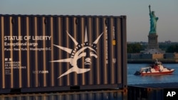 A container carrying a replica of the Statue of Liberty, left, passes in front of the full-sized Statue of Liberty as it arrives from France on a container ship in New York, June 30, 2021.