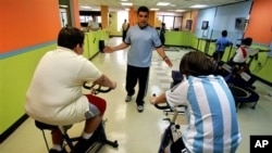 In this 2007 file photo, fitness expert Jose Ortiz helps train overweight boys on stationary bikes in Puerto Rico. (AP Photo/Brennan Linsley)