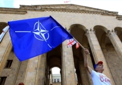 FILE - A NATO supporter waves a NATO flag during a rally in front of Georgia's Parliament building in Tbilisi, Georgia, July 6, 2019.