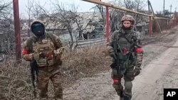 Dua tentara unit teknik militer Rusia berjalan saat sedang bertugas untuk membersihkan ranjau di Kota Avdiivka, Ukraina timur. (Foto: via AP)