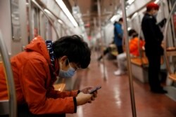A man wearing a face mask checks his mobile phone while riding a subway in the morning after the extended Lunar New Year holiday caused by the coronavirus outbreak, in Beijing, Feb. 10, 2020.