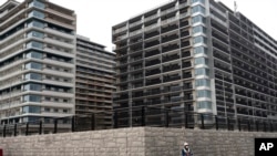 FILE - A guard stands in front of apartment buildings at the Athletes Village for the Tokyo 2020 Olympics, in Tokyo, March 23, 2020.