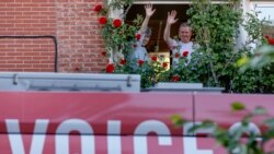 A couple wave from a window as they greet a bus delivering a loudspeaker message from family and friends in Brussels, Wednesday, April 22, 2020. (AP Photo/Olivier Matthys)