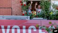 A couple wave from a window as they greet a bus delivering a loudspeaker message from family and friends in Brussels, Wednesday, April 22, 2020. (AP Photo/Olivier Matthys)