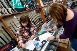 Andrea Schry, right, fills out the buyer part of legal forms to buy a handgun as shop worker Missy Morosky fills out the vendors parts after Dukes Sport Shop reopened, March 25, 2020, in New Castle, Pa.