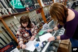 Andrea Schry, right, fills out the buyer part of legal forms to buy a handgun as shop worker Missy Morosky fills out the vendors parts after Dukes Sport Shop reopened, March 25, 2020, in New Castle, Pa.