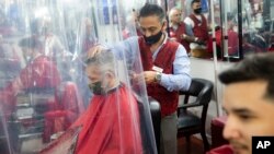 Peter Shamuelov, center, wears a protective mask as he gives a haircut to a customer at Ace of Cuts barbershop, Monday, June 22, 2020, in New York. For the first time in three months, New Yorkers will be able to dine out, though only at outdoor tables. (AP Photo/John Minchillo)