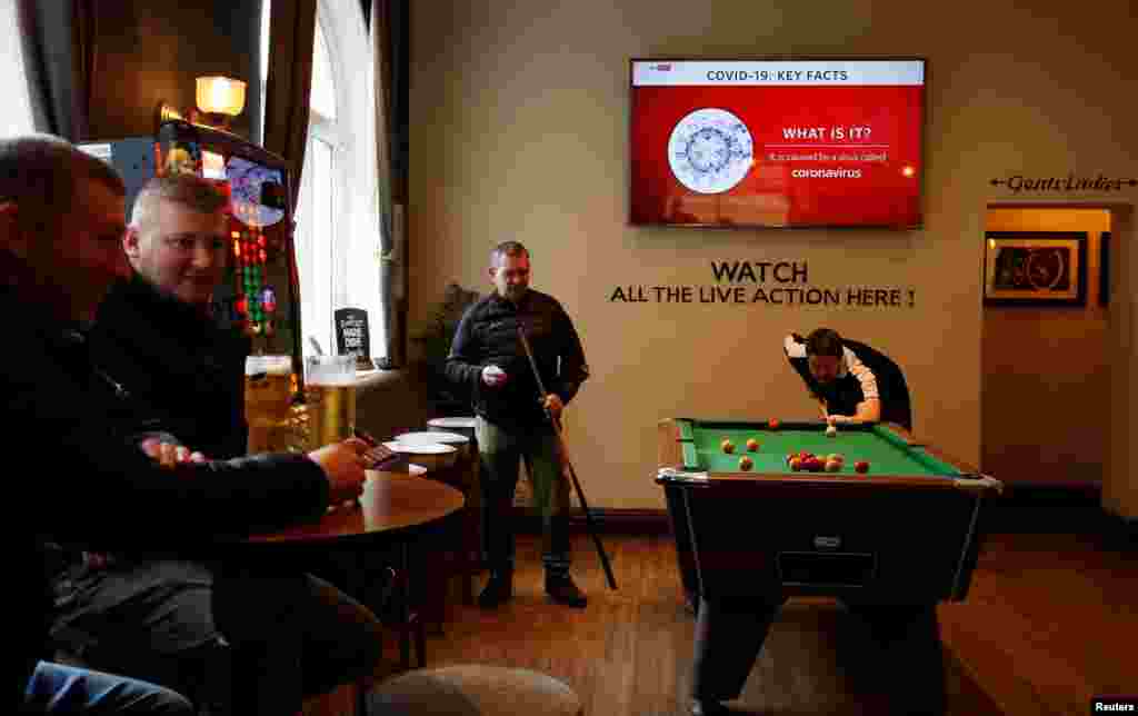 People play pool as a television shows news about the coronavirus outbreak in a pub in Liverpool, Britain.