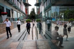 People walk by a shopping mall reflected in a window of a subway station in Shenzhen, China's Guangdong province, Oct. 31, 2019. China's factory activity shrank more sharply than expected in October amid weak consumer demand and a tariff war.