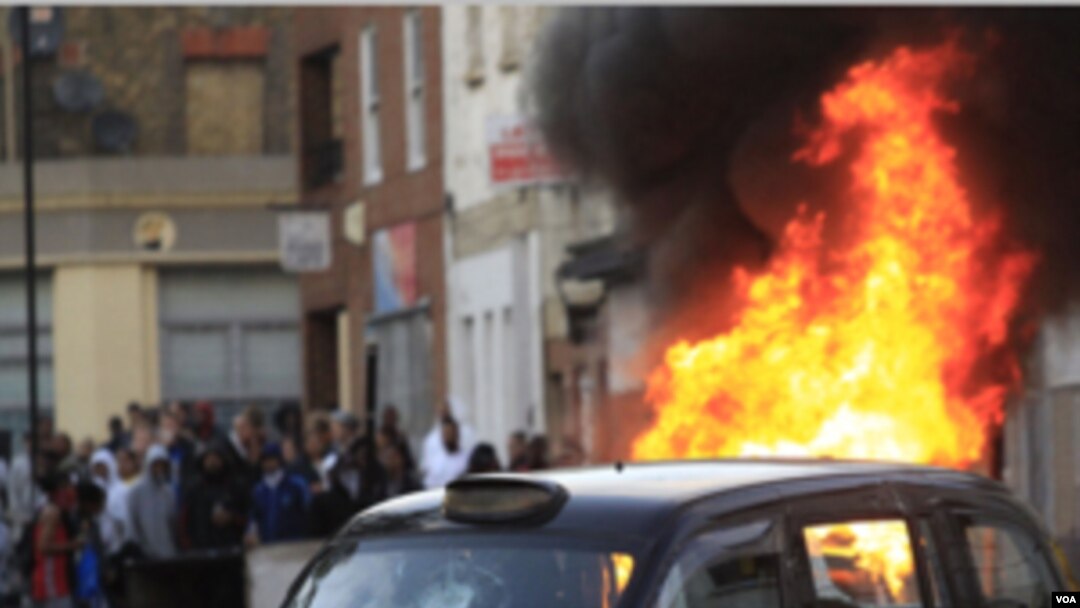 Sebuah mobil di belakang taksi di gambar ini dibakar oleh massa di Hackney, London timur, Senin (8/8).