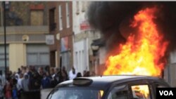 Sebuah mobil di belakang taksi di gambar ini dibakar oleh massa di Hackney, London timur, Senin (8/8).