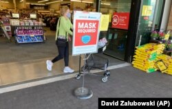 In this May 19, 2021, photo, a shopper pushes her basket filled with purchases past a sign warning of the need to wear face masks while in a food store in Aurora, Colorado. (AP Photo/David Zalubowski)