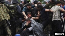 Migrants fall as they make their way through police to cross Greece's border into Macedonia near Gevgelija, Macedonia, Aug. 22, 2015. 