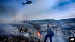 San Diego firefighters knock down a small brush along a hillside over the Mission Valley Shopping Mall in San Diego on Jan. 21, 2025.