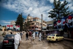 FILE - Workers disinfect the streets to prevent the spread of coronavirus in Qamishli, Syria, March 24, 2020. Posters show Syrian President Bashar al-Assad.