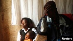An HIV-AIDS patient (R) places her hand on her forehead during a visit by a caregiver at her home in Matero township on the outskirts of Lusaka, Zambia, April 17, 2012.
