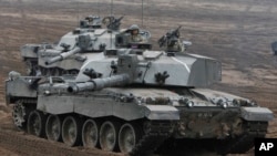 FILE - British troops atop tanks salute as they take part in joint military exercises with Polish troops in Swietoszow, Poland, Nov. 21, 2014.