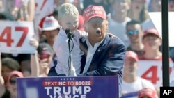 Republican presidential nominee former President Donald Trump holds his grandson Luke Trump as he speaks at a campaign event at Wilmington International Airport in Wilmington, N.C., Sept. 21, 2024. 