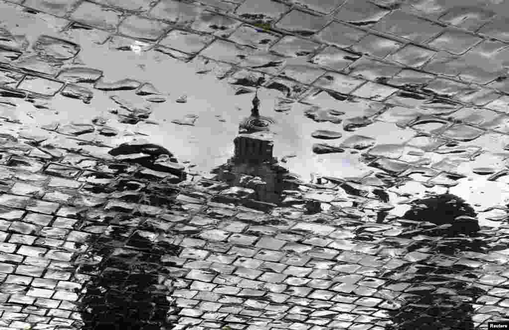 The dome of Saint Peter&#39;s Basilica is reflected in a water puddle while workers prepare the weekly audience of Pope Benedict XVI in Saint Peter&#39;s Square at the Vatican.